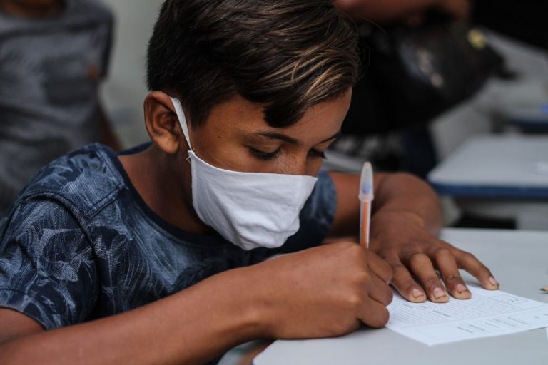 Aluno está com máscara escrevendo num papel