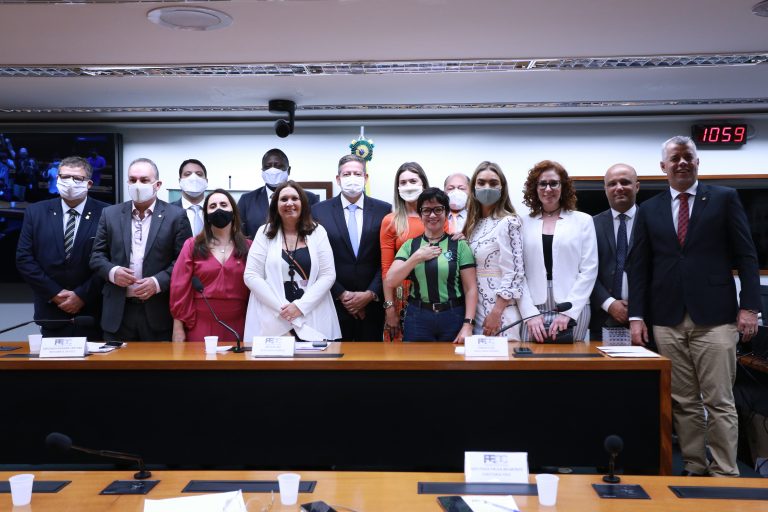 Vários deputados estão em pé, posando para a foto, atrás de uma mesa