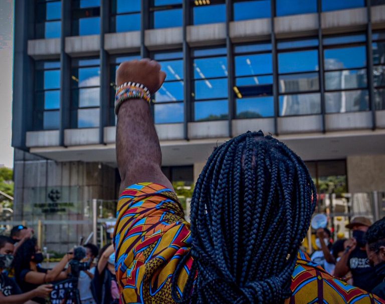 Homem negro está de costas com a mão erguida com o punho fechado