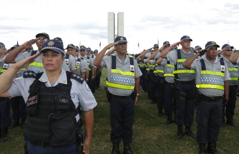 Policiais militares estão em pé, batendo continência, no gramado em frente ao Congresso Nacional