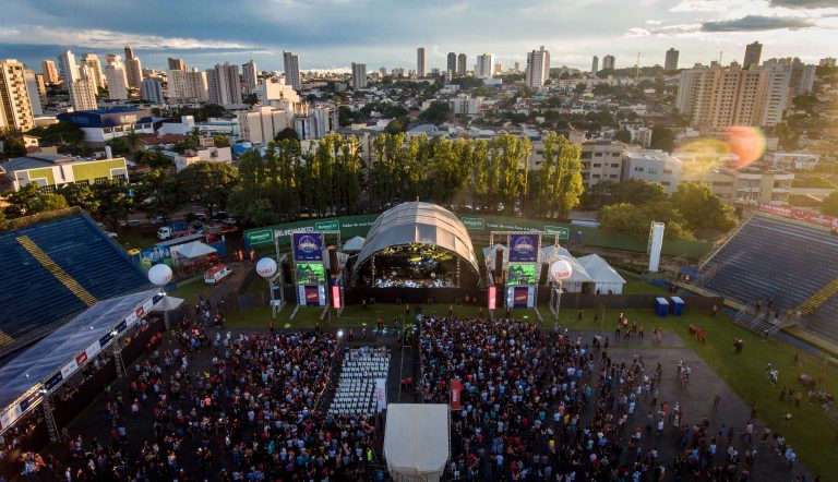Show de banda de música. Foto mostra um palco montado no gramado de um estádio e na frente uma multidão de pessoas