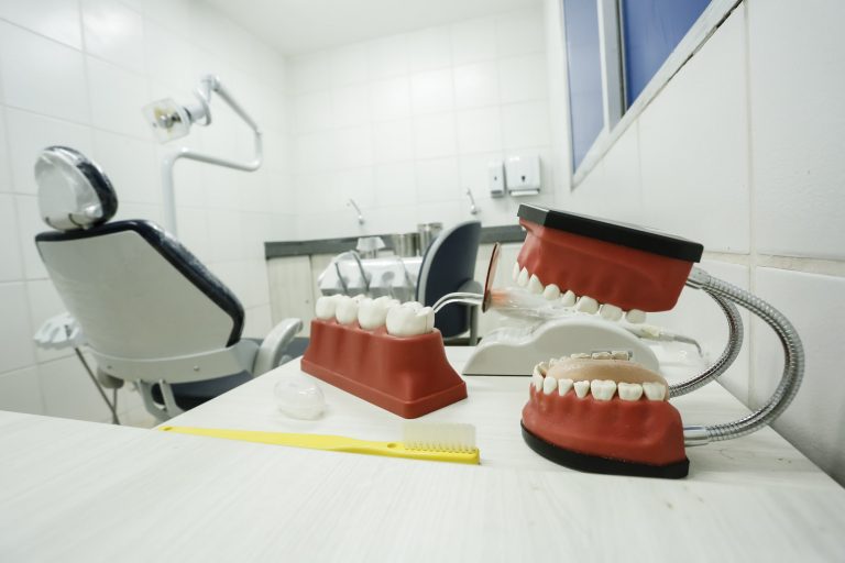 Consultório odontológico vazio. Em cima da mesa há uma escova de dentes e uma maquete de uma boca com dentes