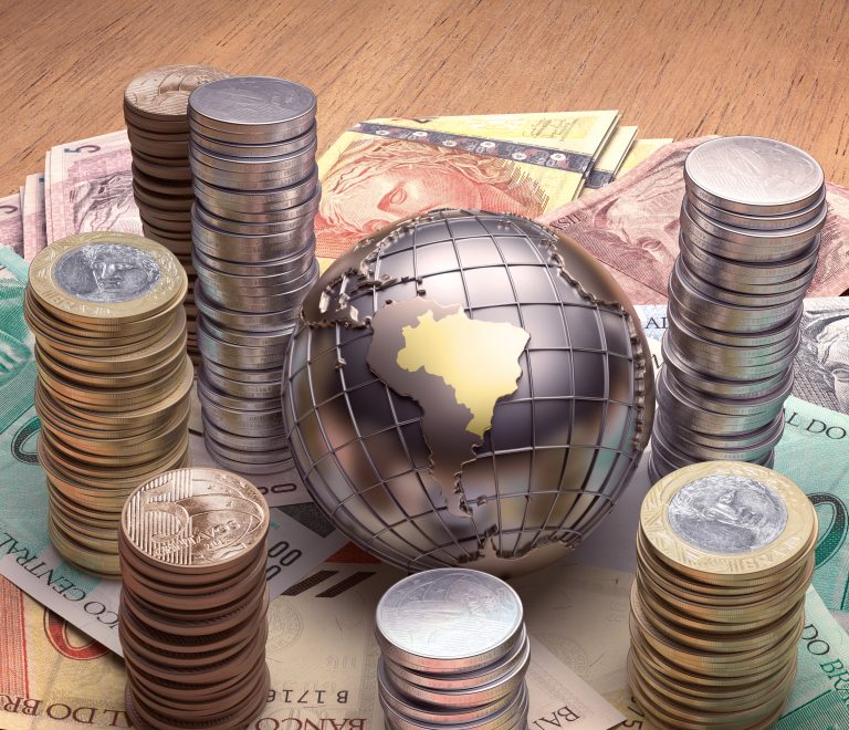 Moedas e cédulas de dinheiro estão em volta de um globo terrestre onde se destaca o Brasil