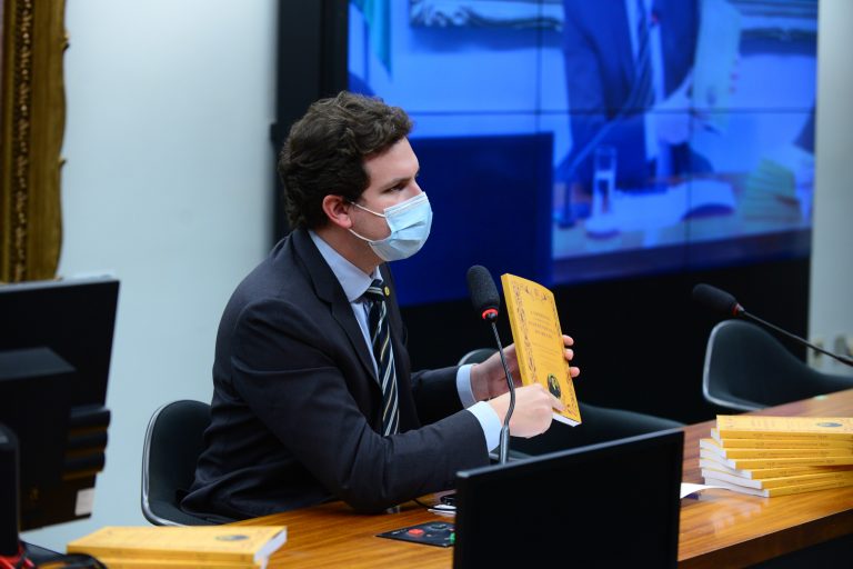 Deputado Enrico Misasi está sentado segurando um livro de capa amarela