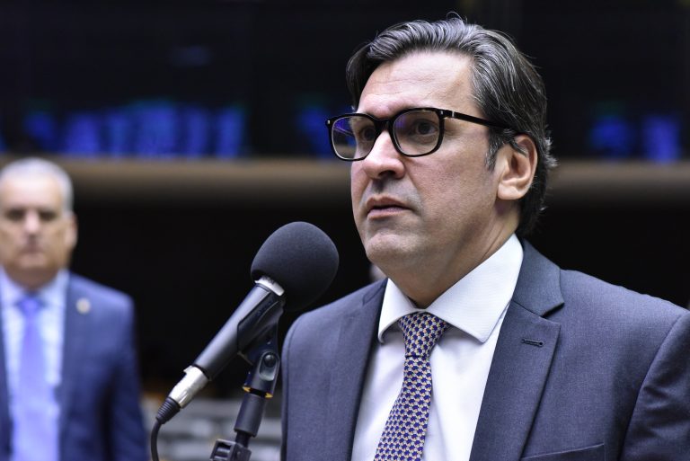 Deputado Isnaldo Bulhões Jr. fala ao microfone. Ele é um homem branco, tem cabelo escuro e usa óculos