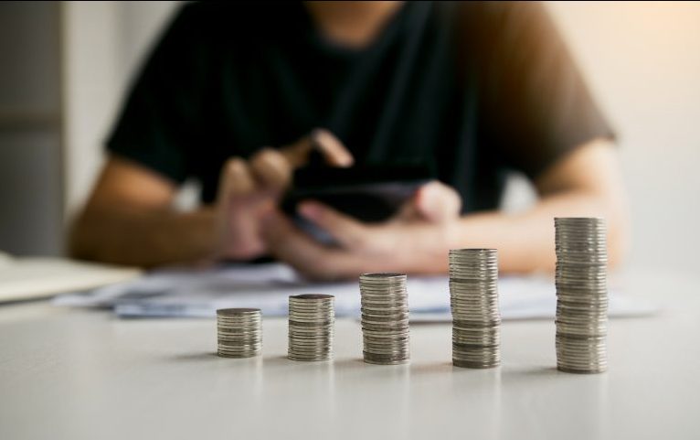Moedas empilhadas e pessoa fazendo contas