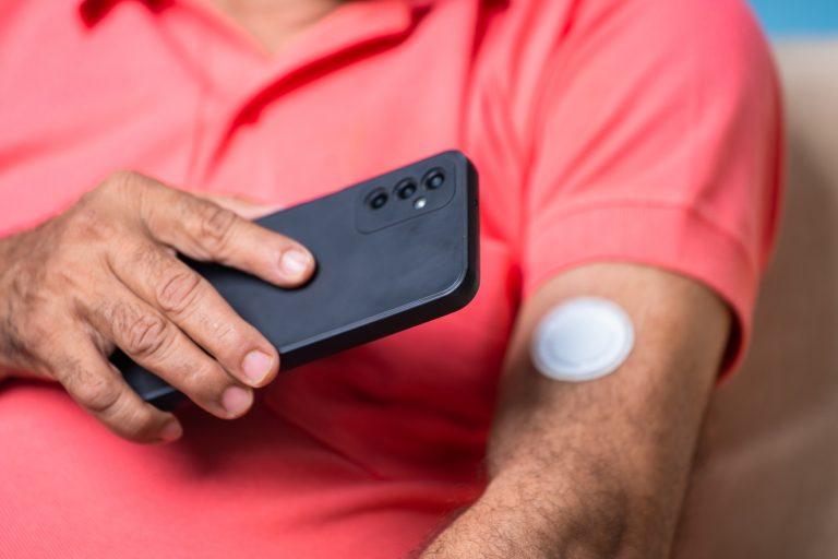 Um homem com um adesivo no braço aproxima o celular do adesivo