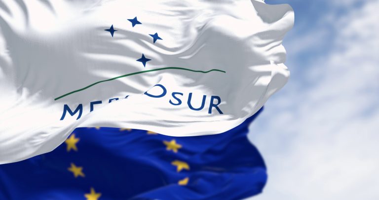Bandeiras do Mercosul e da União Europeia tremulam num céu com nuvens