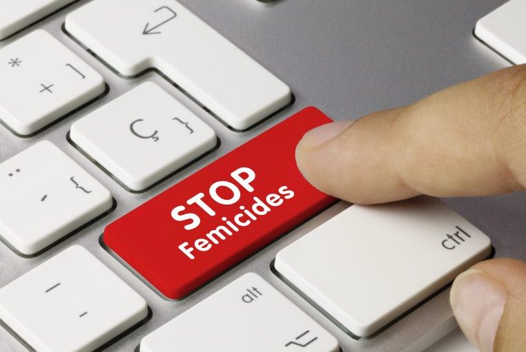 Dedo aperta uma tecla vermelha de teclado de computador onde se lê: "Stop feminicides"
